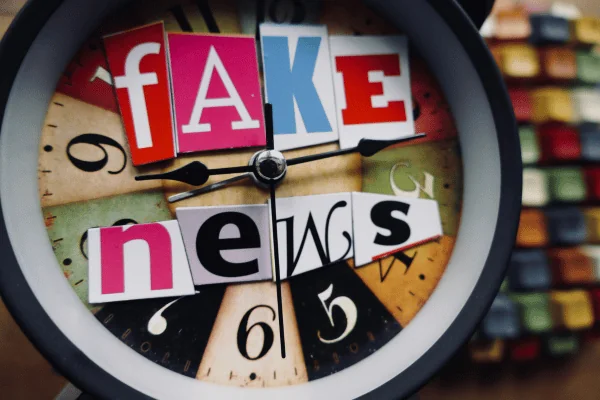 Uhr mit ausgeschnittenen Buchstaben, die den Schriftzug Fake News bilden.